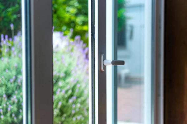 Opened door of a family home. Lock of the sliding door with the yard of background. White PVC door and double glass.