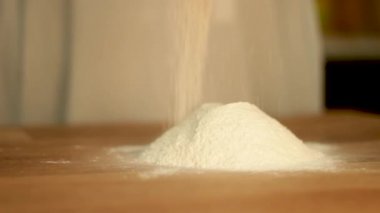 Un parçacıkları masaya serpiştirip tepeyi oluşturuyor. Fırında ya da ev mutfağında hamur yoğurmaya hazırlık. Pişirme malzemeleri. Beyaz toz, kara buğday düşüyor. Hamur işi, ekmek, pasta, makarna