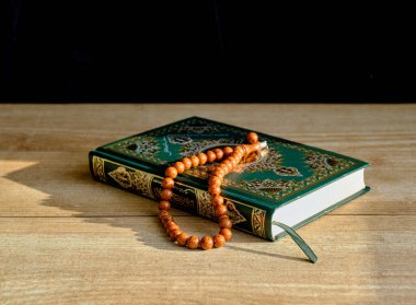 Yeşil ve yaldızlı bir Kur 'an kitabı ve masada duran taştan yapılmış bir tespih..