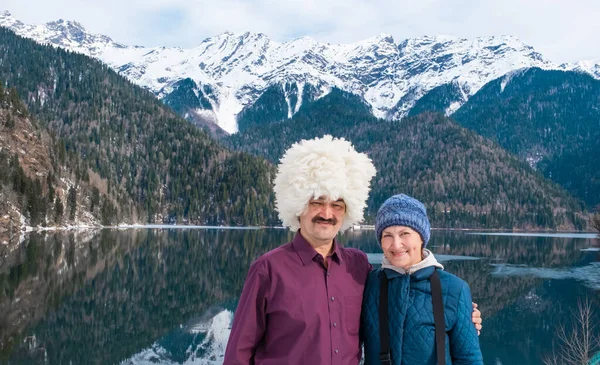 白い羊の帽子をかぶったアジア系の男と白人の妻が 美しい山の風景とアブハジアのリッサ湖を背景にポーズをとっている — ストック写真