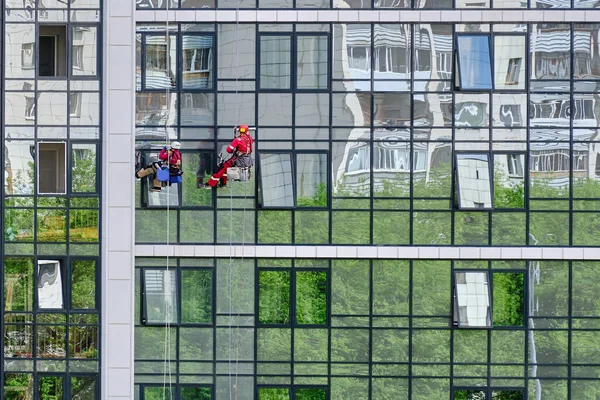 Temizlik servisinden iki endüstriyel tırmanıcı modern bir apartmanın cam cephesini yıkıyor. İp erişimi