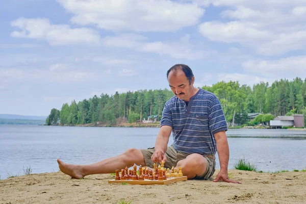 上級アジア人男性はチェスの試合で動き 湖の近くの砂浜に座っています デジタルデトックスコンセプト — ストック写真