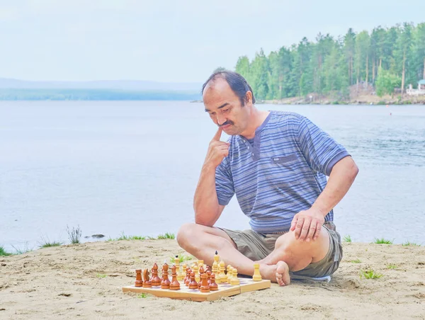 チェスの試合での動きを熟考し 湖の近くのビーチに座っている上級アジア人男性 デジタルデトックスコンセプト — ストック写真
