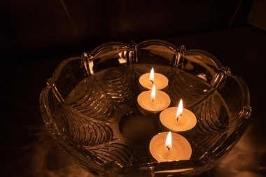 Yüzen mumlarla fal baktırmak. Yanan 4 mum, siyah zemin üzerinde su olan kristal bir kasede yüzer. Öngörü kavramı.