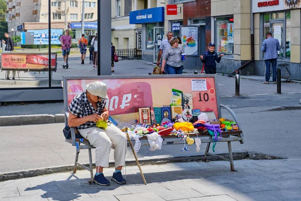 An elderly woman sits on a street bench and knits. — Stock Photo, Image