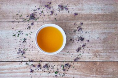 Tahta tahtada beyaz bir fincanda Oregano çayı. Kupa 'nın etrafında çiçekler ve kurumuş kekik yaprakları var. Üst görünüm.