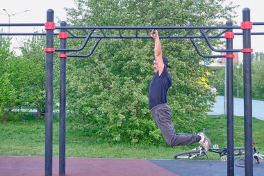 Mutlu kıdemli Asyalı adam şehir parkında bir çiçek bitkisinin arka planında antrenman yapıyor. Çapraz direkte asılı duruyor. Yaşam tarzı, sağlıklı alışkanlıklar. Hareket bulanıklığı