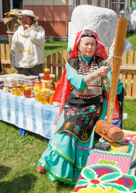 Yekaterinburg, Rusya, 15 Haziran 2019. Bashkir elbiseli bir kadın oturmuş yün örüyor. Şehir parkında geleneksel ulusal tatil Sabantuy.