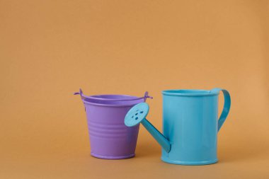 Oyuncak mavi sulama kutusu ve turuncu arka planda mor kova. Mesaj için yer. Tarım kavramı.