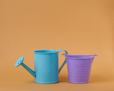 Oyuncak mavi sulama kutusu ve turuncu arka planda mor kova. Mesaj için yer. Tarım kavramı.