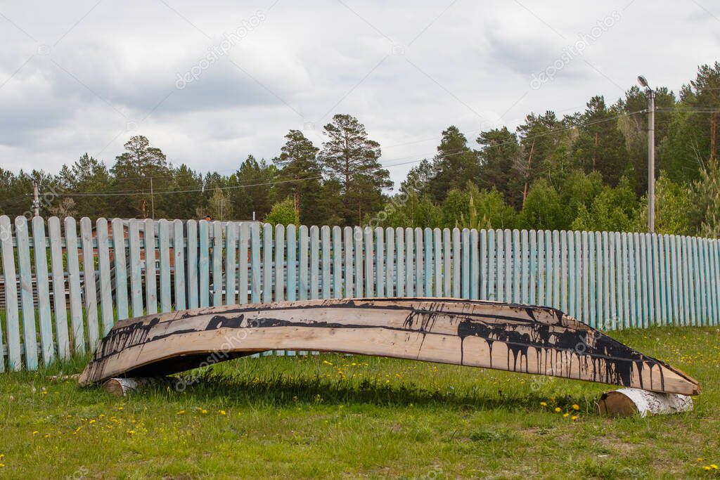 New wooden tarred boat of pine lies upside down in a clearing near the fence.