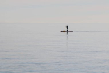 Küreğiyle sörf tahtasıyla denizi aşan çantalı yalnız bir adam. Minimalizm.