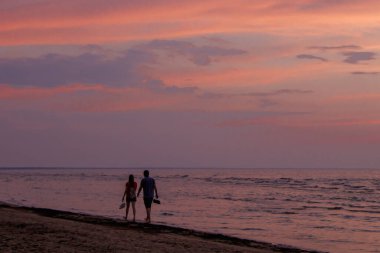 Renkli bir günbatımında deniz kıyısında yalınayak yürüyen bir çift. Jurmala plajı, Baltık kıyısı, Letonya.