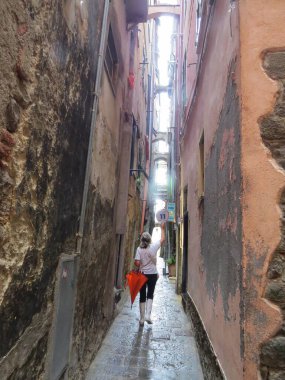 Manarola, İtalya, 30 Temmuz 2014. Yağmurlu bir yaz gününde rehber, kıyı kenti Manarola 'nın dar caddesinde bir tur düzenler. Bir elinde kırmızı bir şemsiye tutuyor.