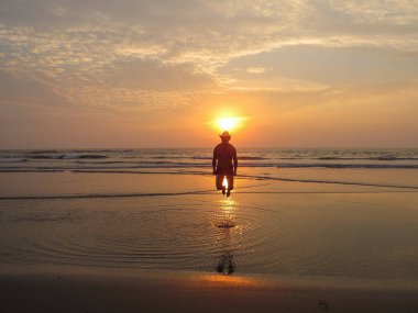 Gün batımında, şapkalı mutlu bir adam neşe içinde sudan atlıyor.