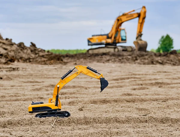 Žlutý Hračka Crawler Bagr Pozadí Skutečného Bagru — Stock fotografie