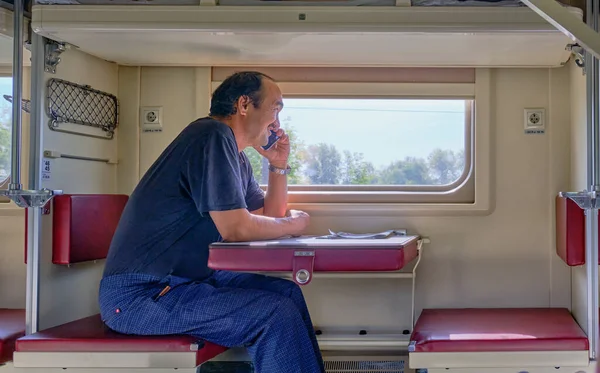 Пожилой человек путешествует на поезде по России. Он сидит в купе второго вагона и разговаривает по мобильному телефону.. — стоковое фото