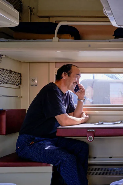 Пожилой человек путешествует на поезде по России. Он сидит в купе второго вагона и разговаривает по мобильному телефону.. — стоковое фото