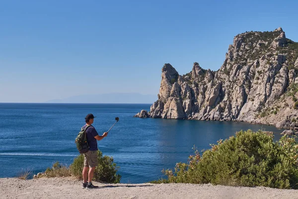 Black Sea coast. An Asian elderly man with a backpack takes a selfie against the background of the Blue Bay on the tourist route Golitsyn trail