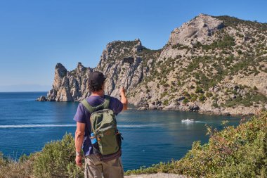 Karadeniz kıyısı, Kırım yarımadası. Sırt çantalı bir Asyalı son sınıf öğrencisi Golitsyn patikasındaki Blue Bay 'in arka planında akıllı bir telefonla fotoğraf çekiyor. Botanik rezervi Yeni Dünya