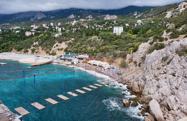 Yalta yakınlarındaki Karadeniz kıyısındaki Diva kayasına asma köprü. Simeiz kasabasının panoraması.