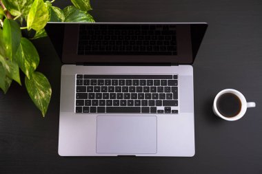 Ortasında bir fincan kahve ve çiçekle çevrili dizüstü bilgisayarla çalışma alanının en üst görüntüsü