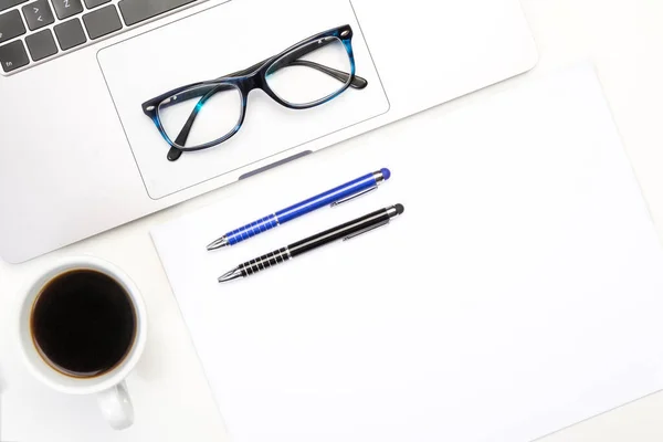 Top view of workspace, laptop, glasses and pens, cup of coffee and white paper A4.