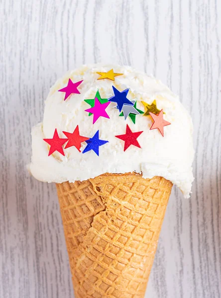 Cono de helado decorado con estrellas sobre un fondo de madera blanca. Un cono de helado al estilo oblea. De cerca. — Foto de Stock