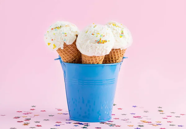 Conos de helado en un cubo azul sobre un fondo rosa decorado con estrellas. Un cono de helado estilo oblea . — Foto de Stock