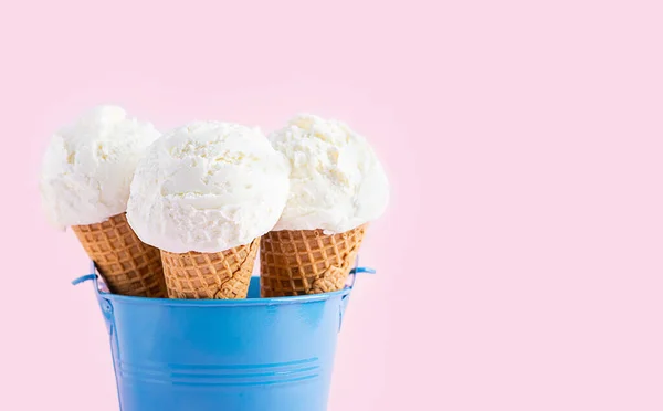 Conos de helado en un cubo azul sobre un fondo rosa. Un cono de helado estilo oblea . — Foto de Stock