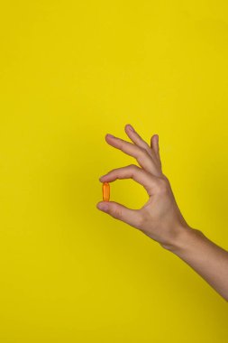 Kızların elindeki uyuşturucu. Genç bir kadın elinde turuncu ilaç kapsülü tutuyor. Sarı arka planda vitamin. Sağlık hizmeti kavramı. 