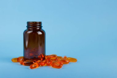 Altın balık yağı kapsülleri, omega 3, cam kavanozda D vitamini mavi arka planda izole edilmiş. Sağlık hizmeti kavramı.