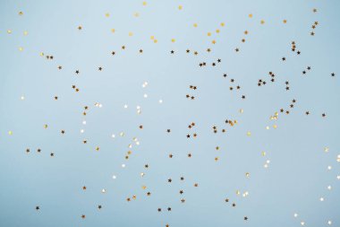 Pastel mavi renk şenlik arka planında altın yıldızların parıltısı konfetisi. Metin ve tasarım için kopyalama alanı olan düz stil.