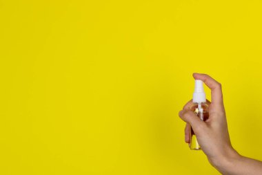 Kadın elinin sarı arka planında şeffaf bir dezenfektan şişesi.. 