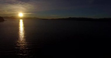 Dağın tepesindeki güneş, sarı ışığını Nahuel Huapi Gölü 'ne yansıtıyor.