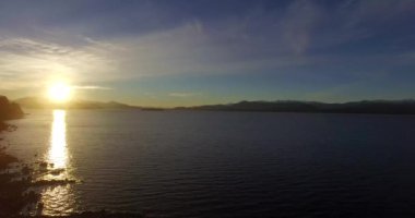 Dağın tepesindeki güneş, sarı ışığını Nahuel Huapi Gölü 'ne yansıtıyor.