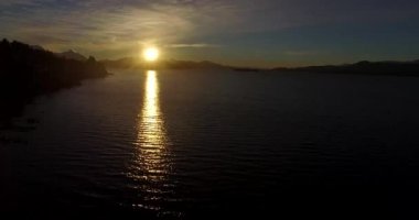 Dağın tepesindeki güneş, sarı ışığını Nahuel Huapi Gölü 'ne yansıtıyor.