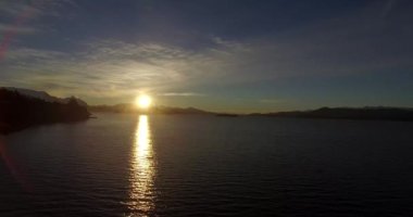 Dağın tepesindeki güneş, sarı ışığını Nahuel Huapi Gölü 'ne yansıtıyor.