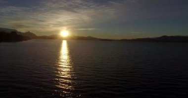 Dağın tepesindeki güneş, sarı ışığını Nahuel Huapi Gölü 'ne yansıtıyor.