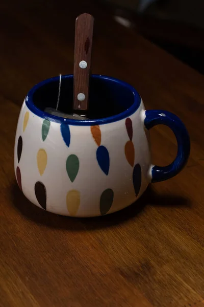 Bir fincan çay, içinde kaşık olan ahşap bir masanın üzerinde.