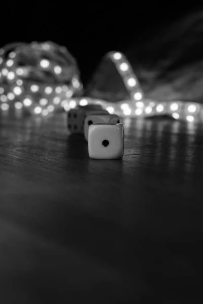 Dices over a table with bright lights behind. The number one up front in black and white.