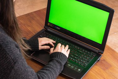 Defterde yazan bir kadın yeşil ekranlı ev ofisini yapıyor. Masanın üzerinde bir bitkiyle