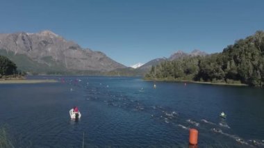 Güneşli bir yaz gününde Nahuel Huapi Gölü 'nü geçen Ironman triatlon yarışmasında yüzücülerin hava görüntüsü. Dağlar ve bitki örtüsüyle çevrili