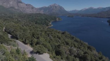 Güneşli bir yaz gününde ağaçlar ve bitki örtüsüyle çevrili Bariloche Arjantin yolunda Ironman triatlonunda yarışan bisikletçinin hava görüntüsü.