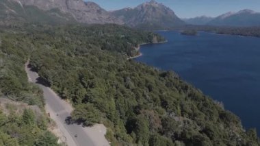 Güneşli bir yaz gününde ağaçlar ve bitki örtüsüyle çevrili Bariloche Arjantin yolunda Ironman triatlonunda yarışan bisikletçinin hava görüntüsü.