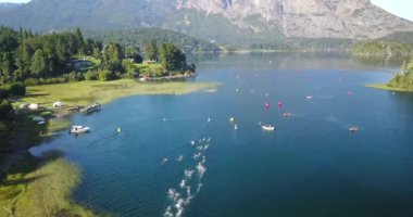Güneşli bir yaz gününde Nahuel Huapi Gölü 'nü geçen Ironman triatlon yarışmasında yüzücülerin hava görüntüsü. Dağlar, bitki örtüsü ve botlarla çevrili.