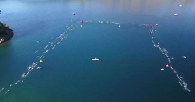 Güneşli bir yaz gününde Nahuel Huapi Gölü 'nü geçen Ironman triatlon yarışmasında yüzücülerin hava görüntüsü. Dağlar, bitki örtüsü ve botlarla çevrili.