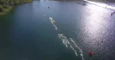 Güneşli bir yaz gününde Nahuel Huapi Gölü 'nü geçen Ironman triatlon yarışmasında yüzücülerin hava görüntüsü. Dağlar, bitki örtüsü ve botlarla çevrili.