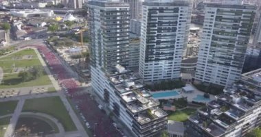 Birçok koşucu, Puerto Madero Arjantin 'in güneşli bir yaz gününde, Buenos Aires' te bir maratonda, şehrin ortasındaki bir sokaktan geçerek nehrin kenarındaki parklarla birlikte koşuyor.