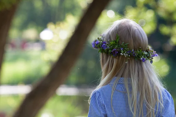 Little blond girl with the wreath of blue wild flowers. Back view. The celebration of Ivan Kupala (St. John Day). Old holiday dedicated to the summer solstice. Selective focus.